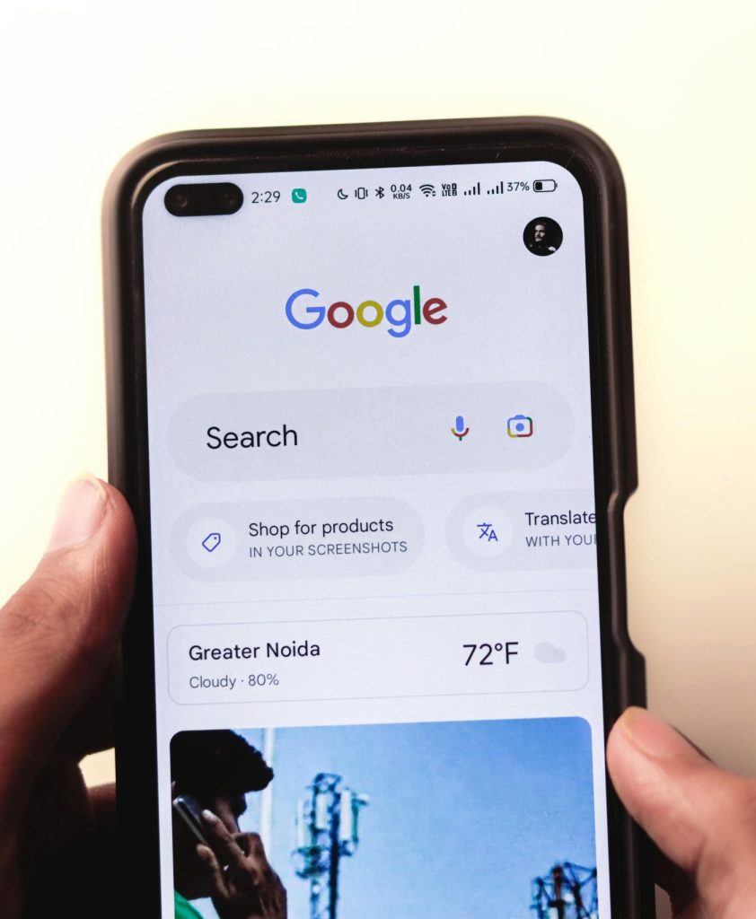 A close-up of a hand holding a smartphone with Google search displayed on the screen.